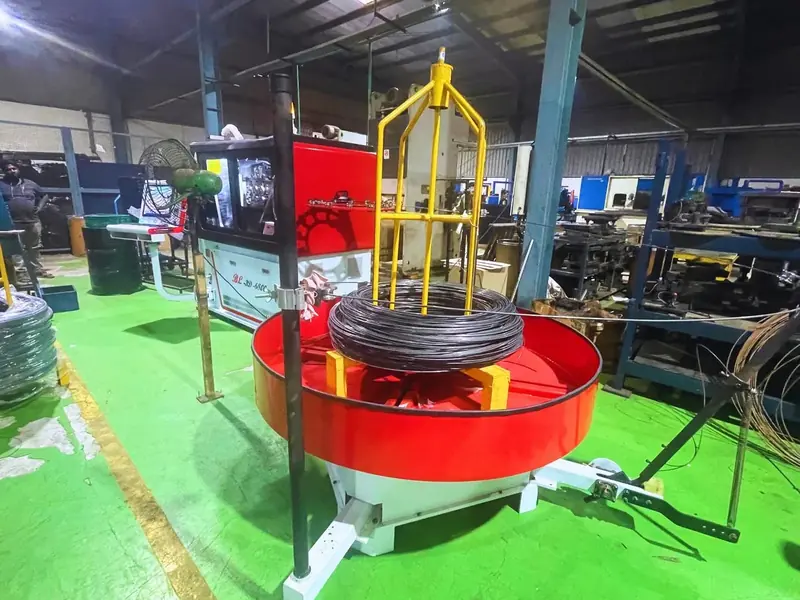 A red wire decoiler holding a coil of wire on the green shop floor