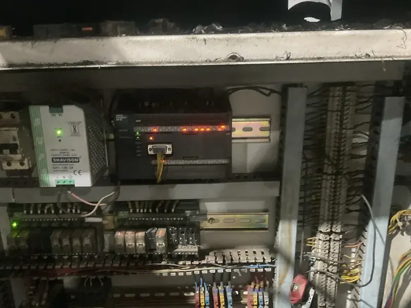 Inside a machine's electrical cabinet at AR Automotive: an Omron PLC with red status lights, a power supply, relays and wiring