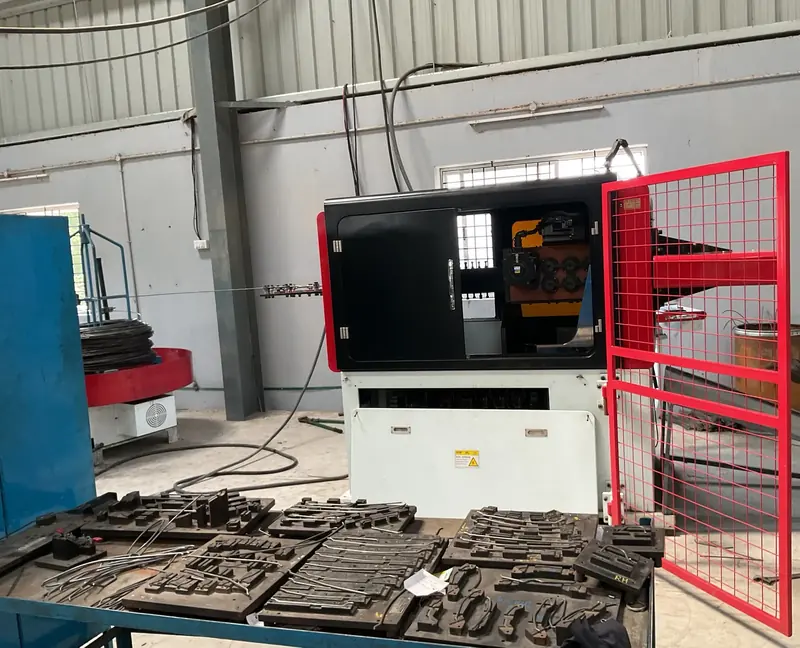A wire forming machine with its red safety door open and tooling plates laid out on a table